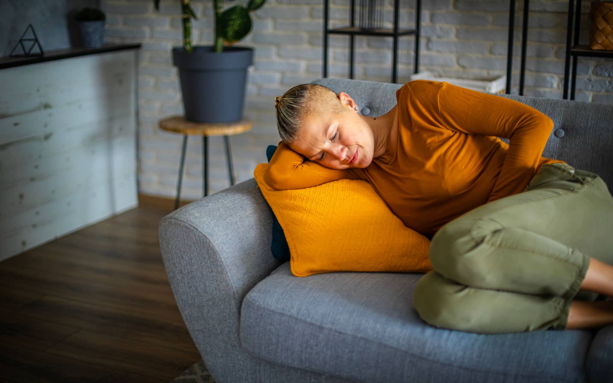 Durchfall bei der Periode: Eine Frau liegt auf dem Sofa und hält ihre Hand schützend vor den Bauch