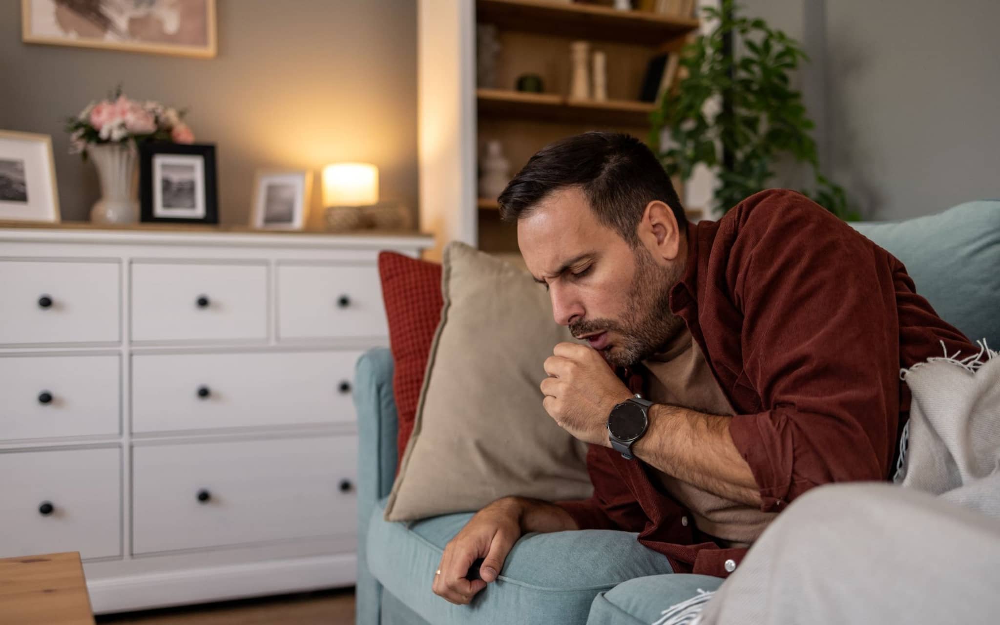 Ein kranker Mann liegt auf dem Sofa und hustet.