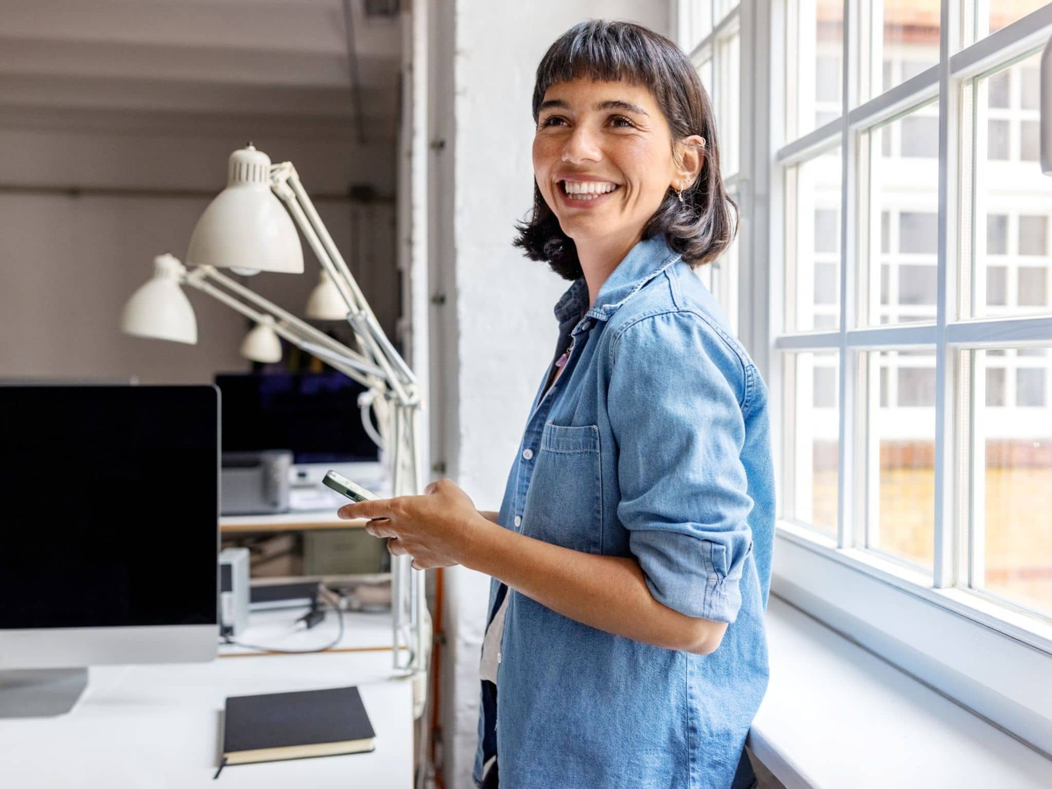 Eine Frau steht im Büro und nutzt die Topfit App auf ihrem Handy.