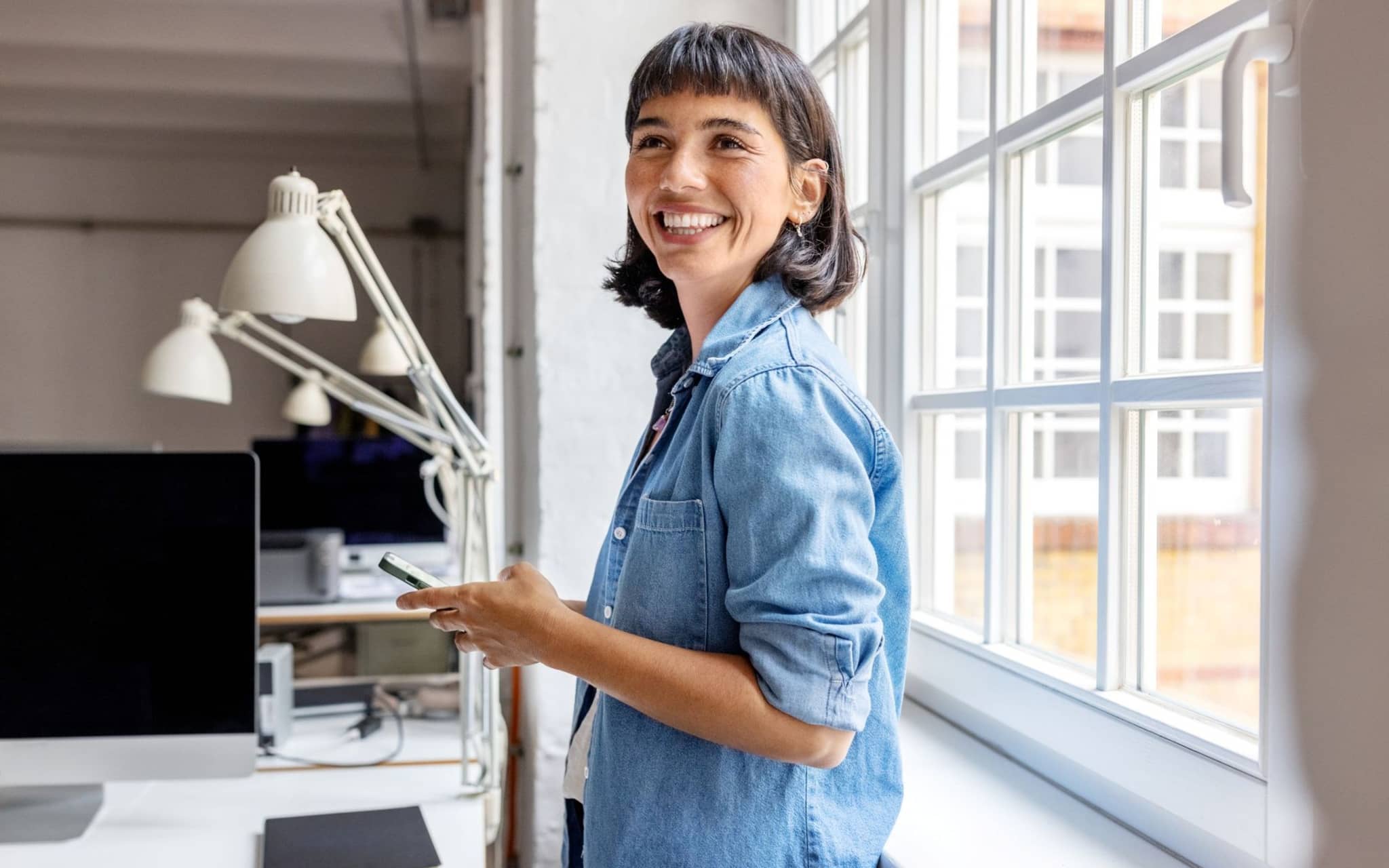 Eine Frau steht im Büro und nutzt die Topfit App auf ihrem Handy.