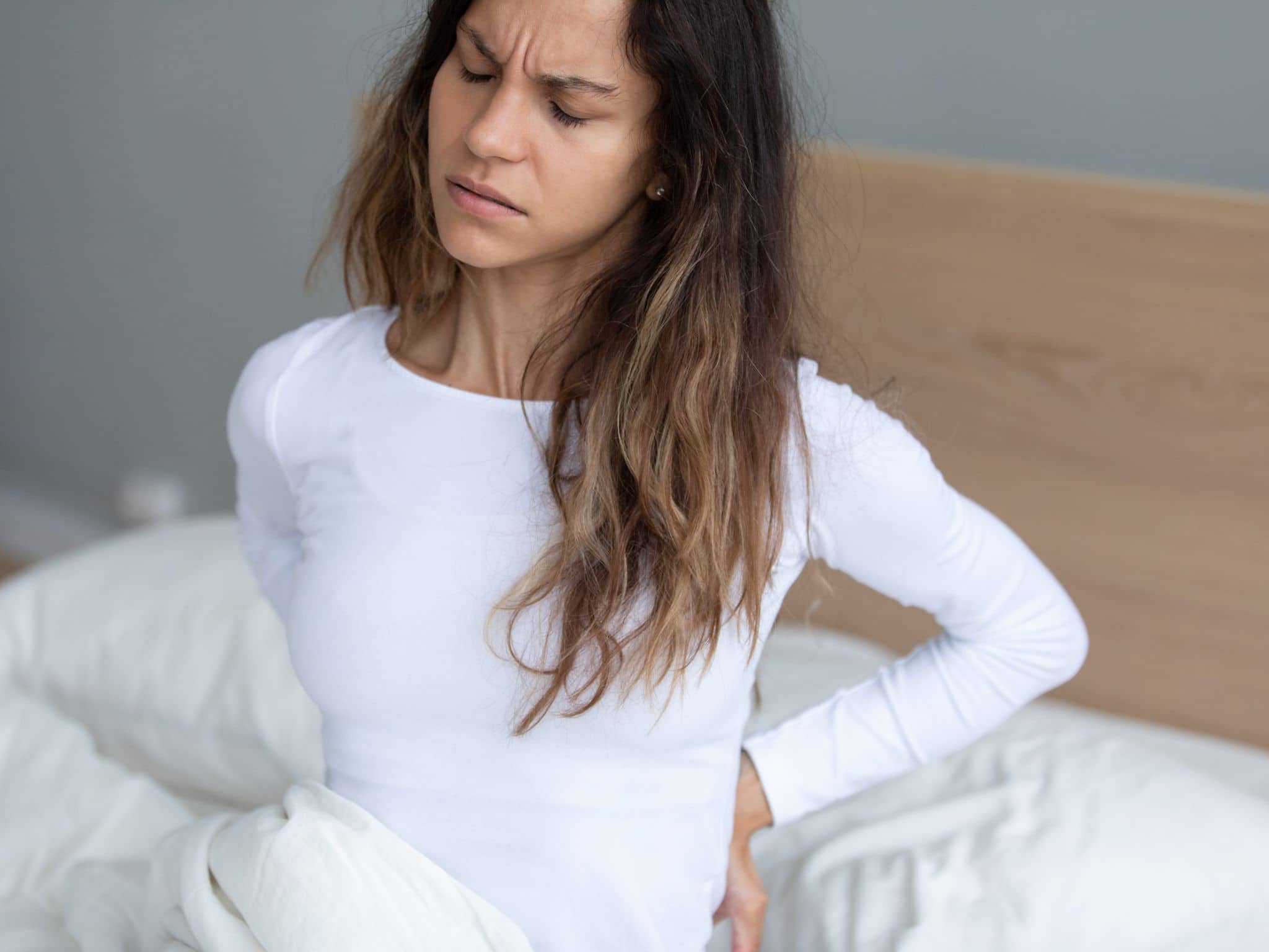 Rückenschmerzen bei der Periode: Eine Frau sitzt auf dem Bett und hält sich den Rücken fest