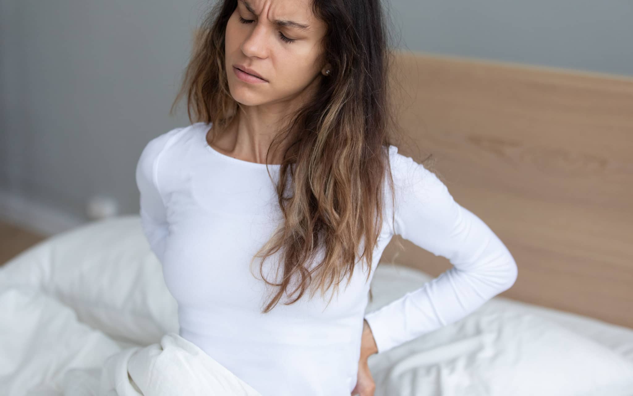 Rückenschmerzen bei der Periode: Eine Frau sitzt auf dem Bett und hält sich den Rücken fest