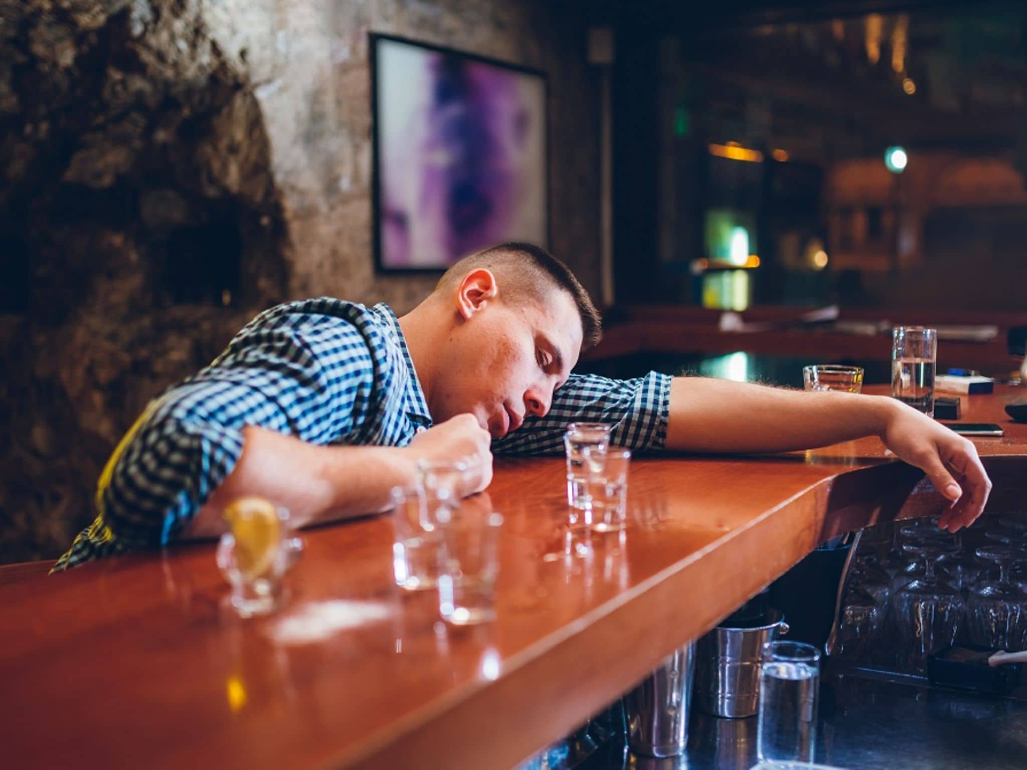 Betrunkener Mann liegt mit Kopf auf Bar neben leeren Schnapsgläsern nach starkem Alkoholkonsum.