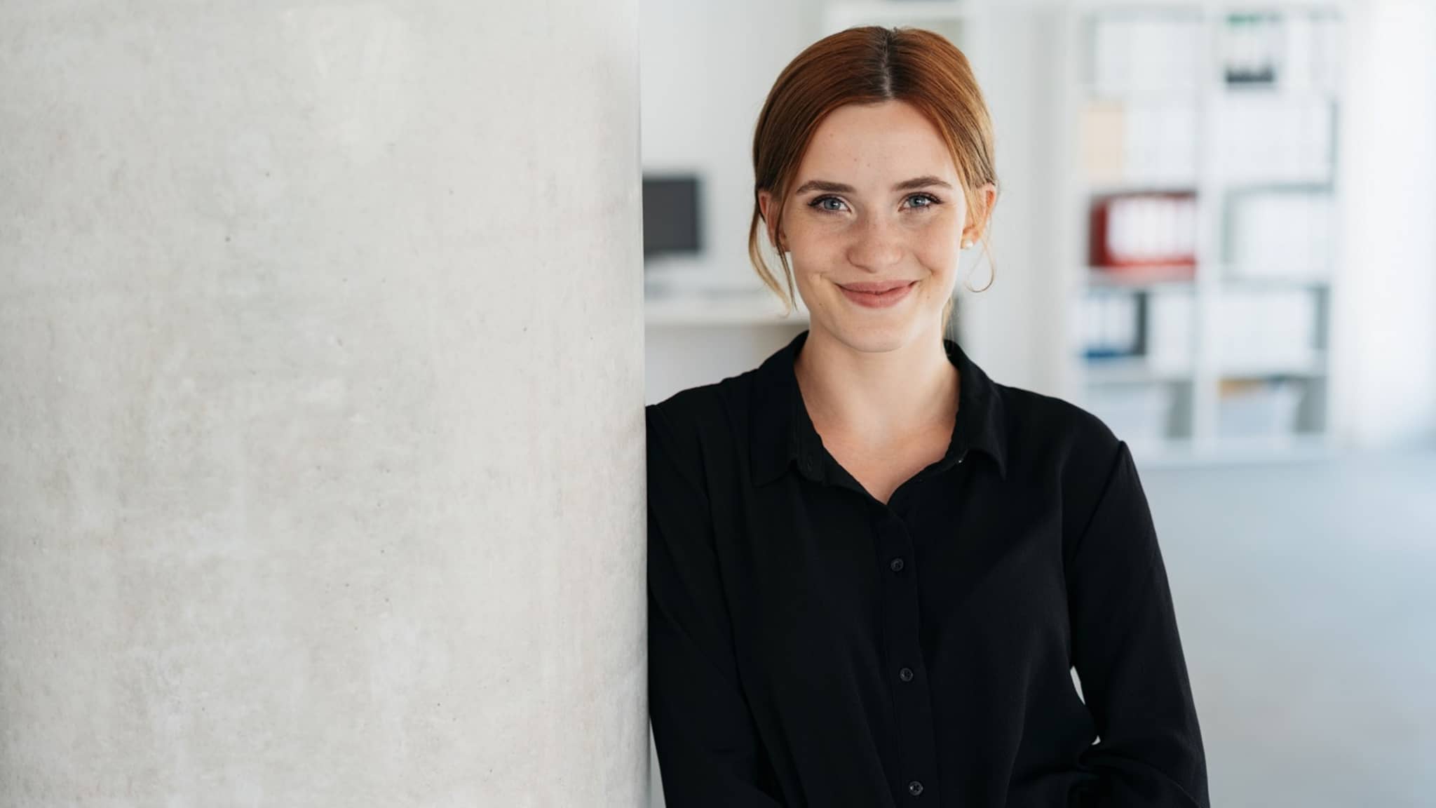 Junge Mitarbeiterin blickt lächelnd in die Kamera.