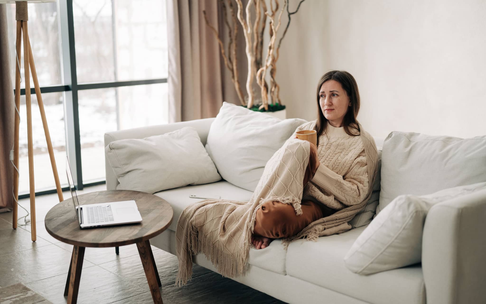 Eine Frau sitzt in eine Decke gekuschelt und einem Sofa und denkt nach
