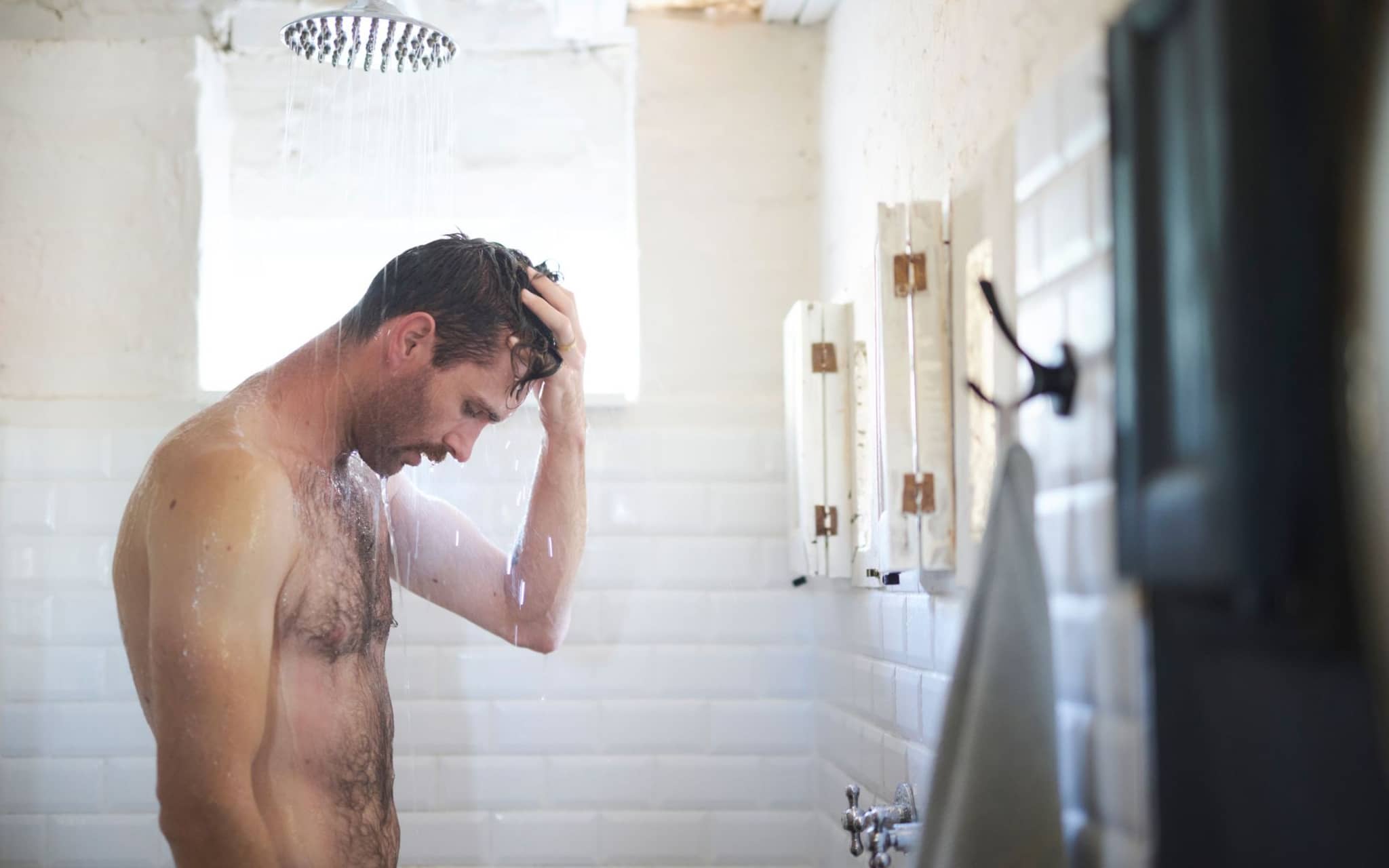 Ein Mann steht unter der Dusche und tastet seine Hoden ab.