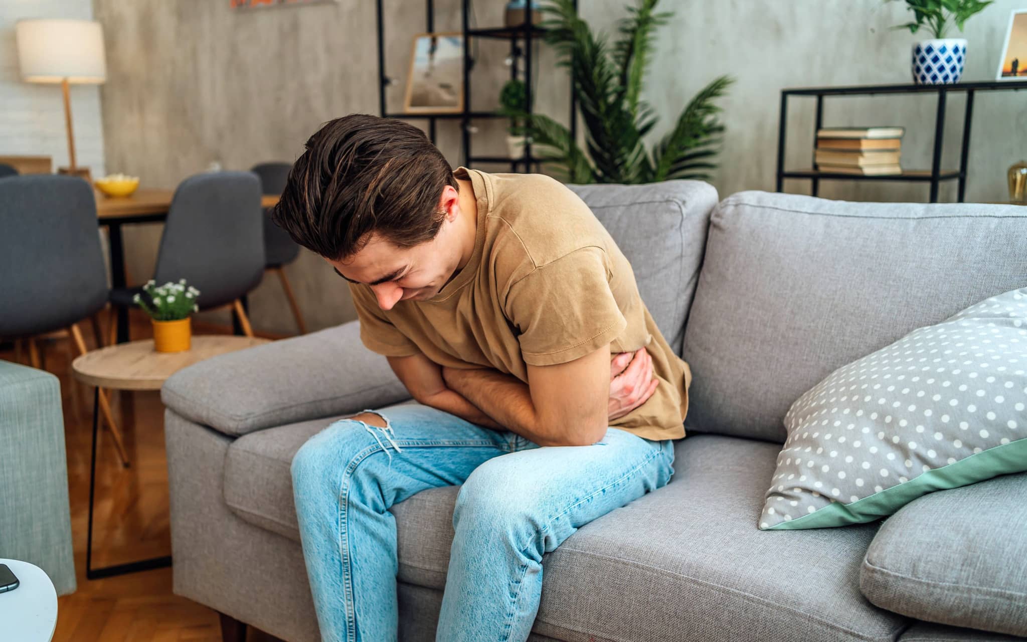 Hodentorsion: Ein Mann sitzt auf einem Sofa und hält sich seinen Bauch vor Schmerzen