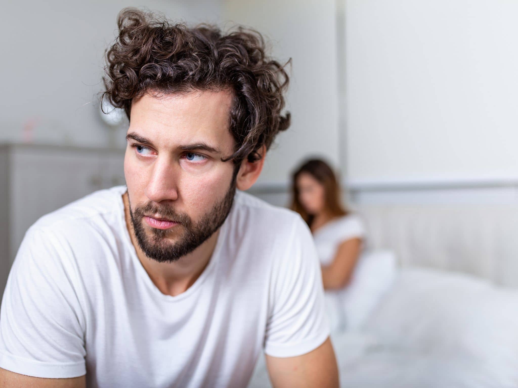 Ein Mann sitzt am Rand eines Bettes und guckt nachdenklich ins Leere