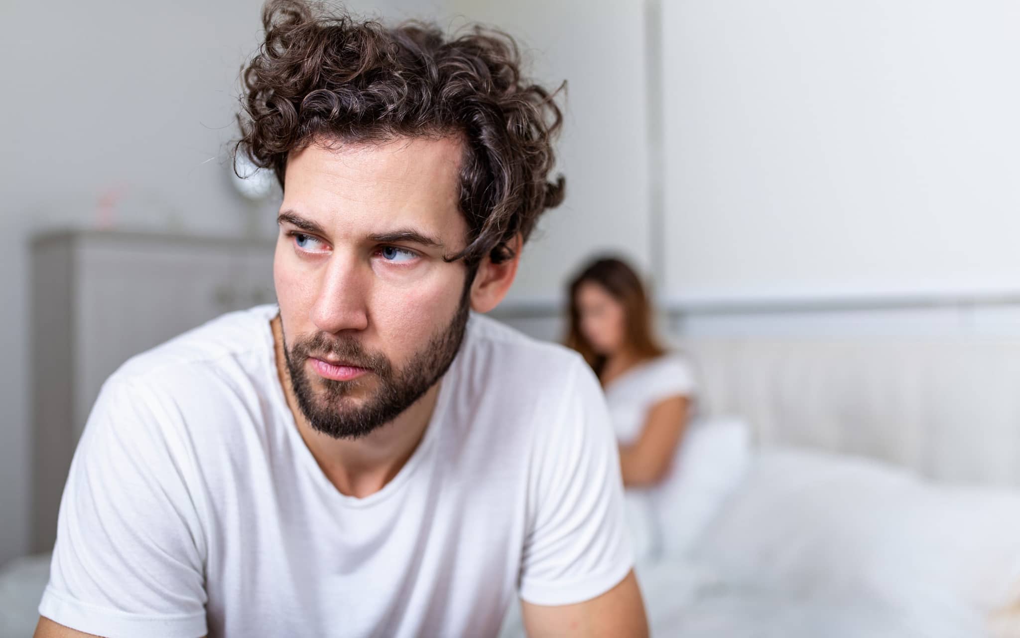 Ein Mann sitzt am Rand eines Bettes und guckt nachdenklich ins Leere