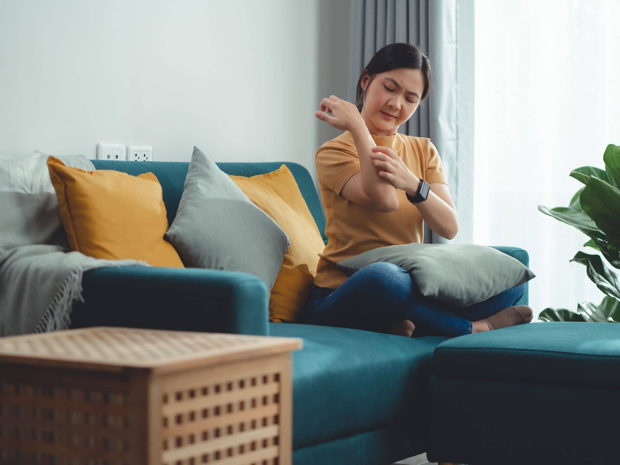Eine Frau sitzt auf einem Sofa und kratzt sich ihre Haut