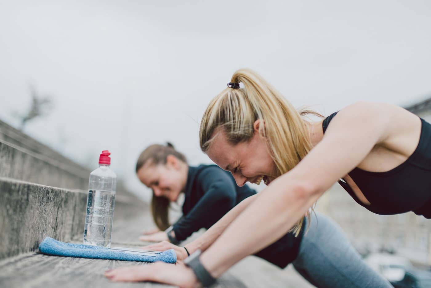 Zwei Freundinnen machen im Freien lachend Liegestütze im Rahmen ihre funktionellen Trainings.