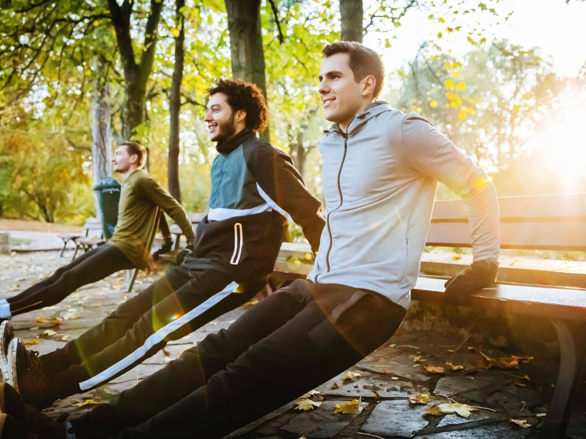 Drei junge Männer machen an einer Parkbank umgedrehte Liegestütz.