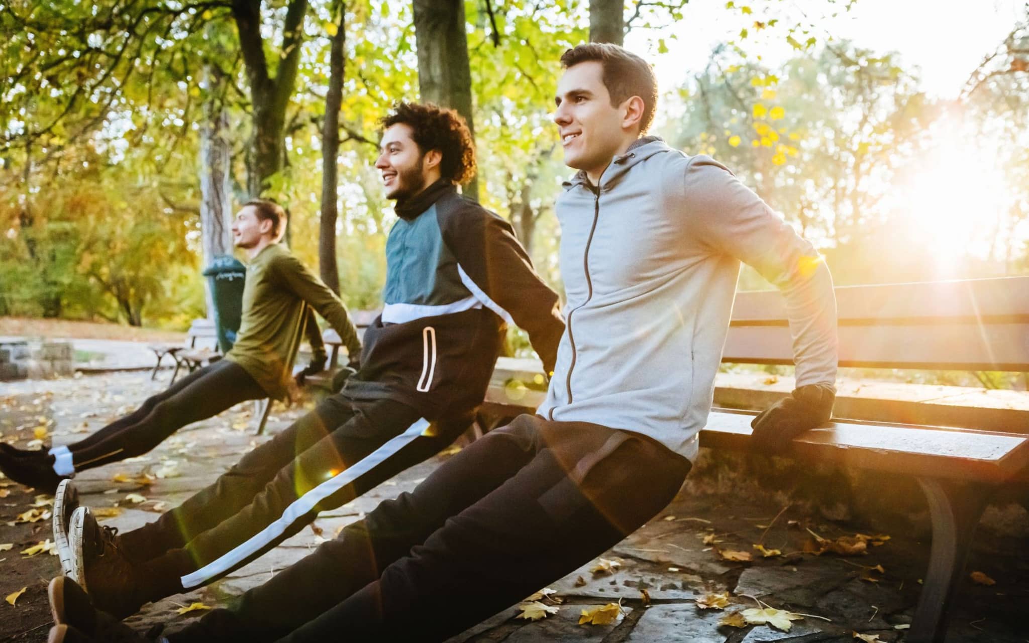 Drei junge Männer machen an einer Parkbank umgedrehte Liegestütz.