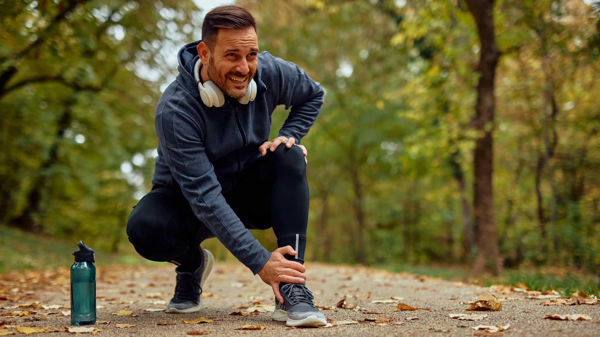 Verletzter Jogger hält sich seinen Knöchel auf einem Parkweg im Herbst