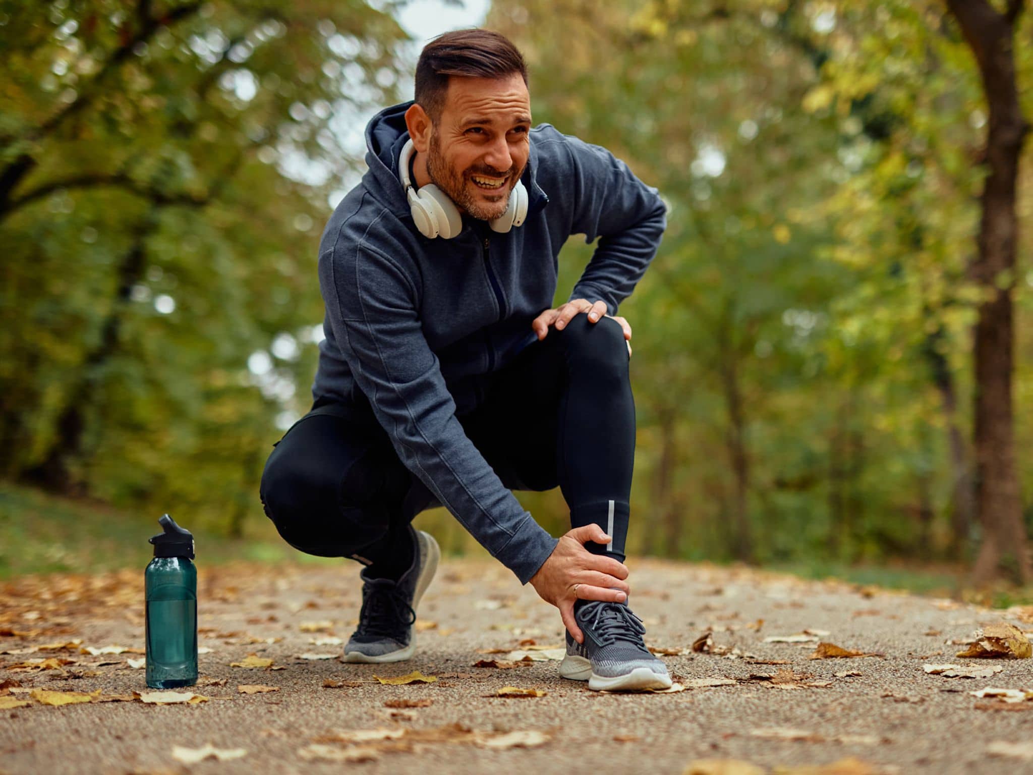 Verletzter Jogger hält sich seinen Knöchel auf einem Parkweg im Herbst