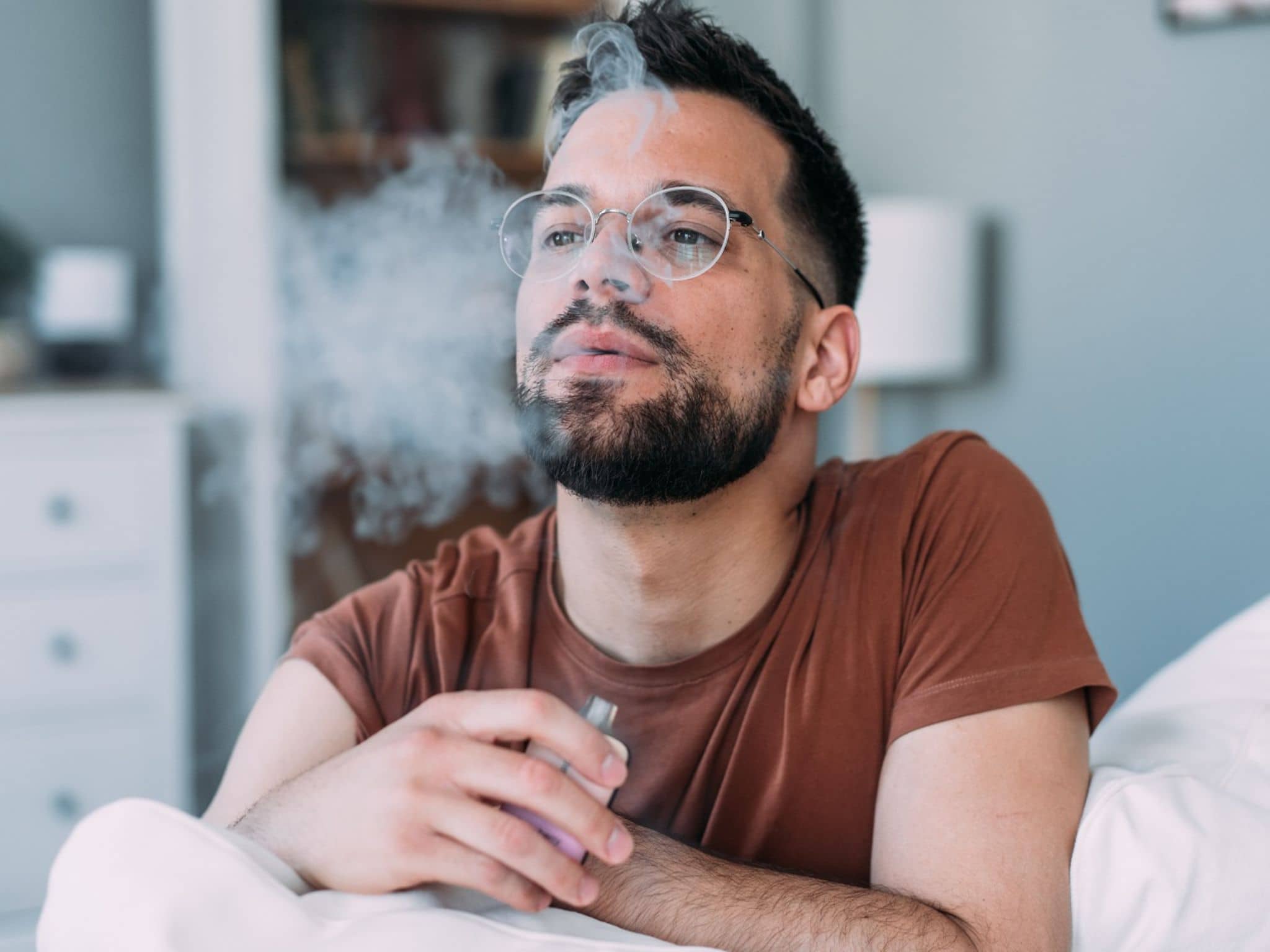 Junger Mann raucht eine E-Zigarette auf dem Sofa.