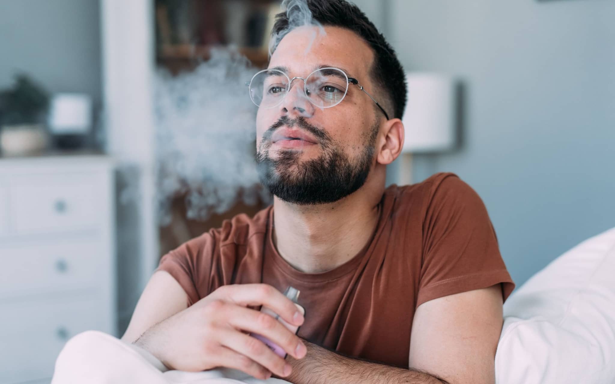 Junger Mann raucht eine E-Zigarette auf dem Sofa.