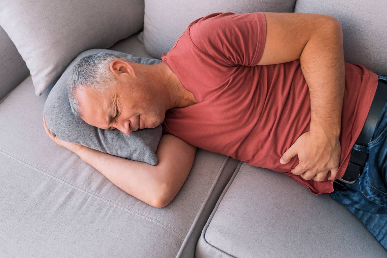Divertikulitis: Mann liegt auf Sofa mit schmerzverzerrtem Gesicht