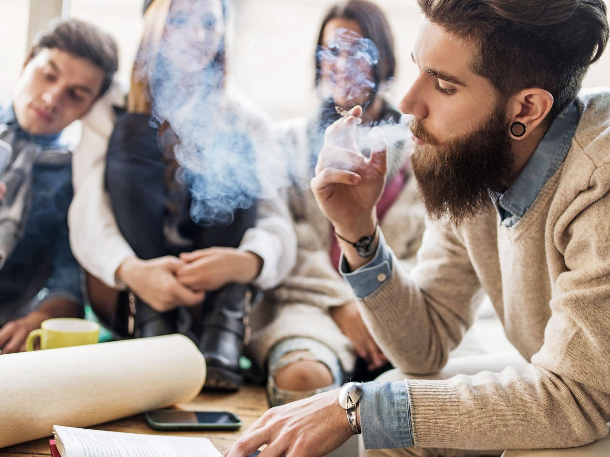 Ein junger Mann raucht in Gegenwart anderer junger Leute auf der Couch.