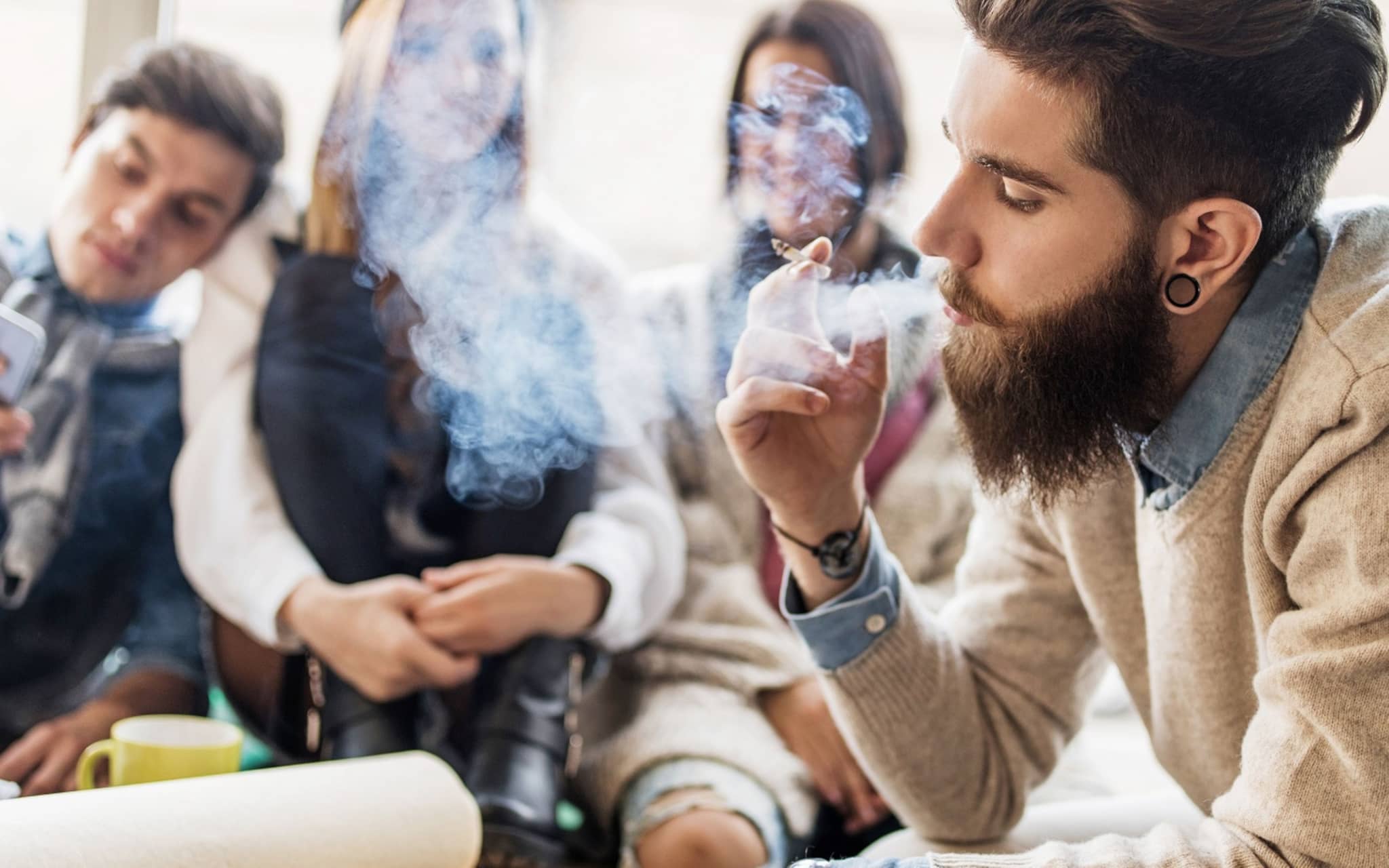 Ein junger Mann raucht in Gegenwart anderer junger Leute auf der Couch.