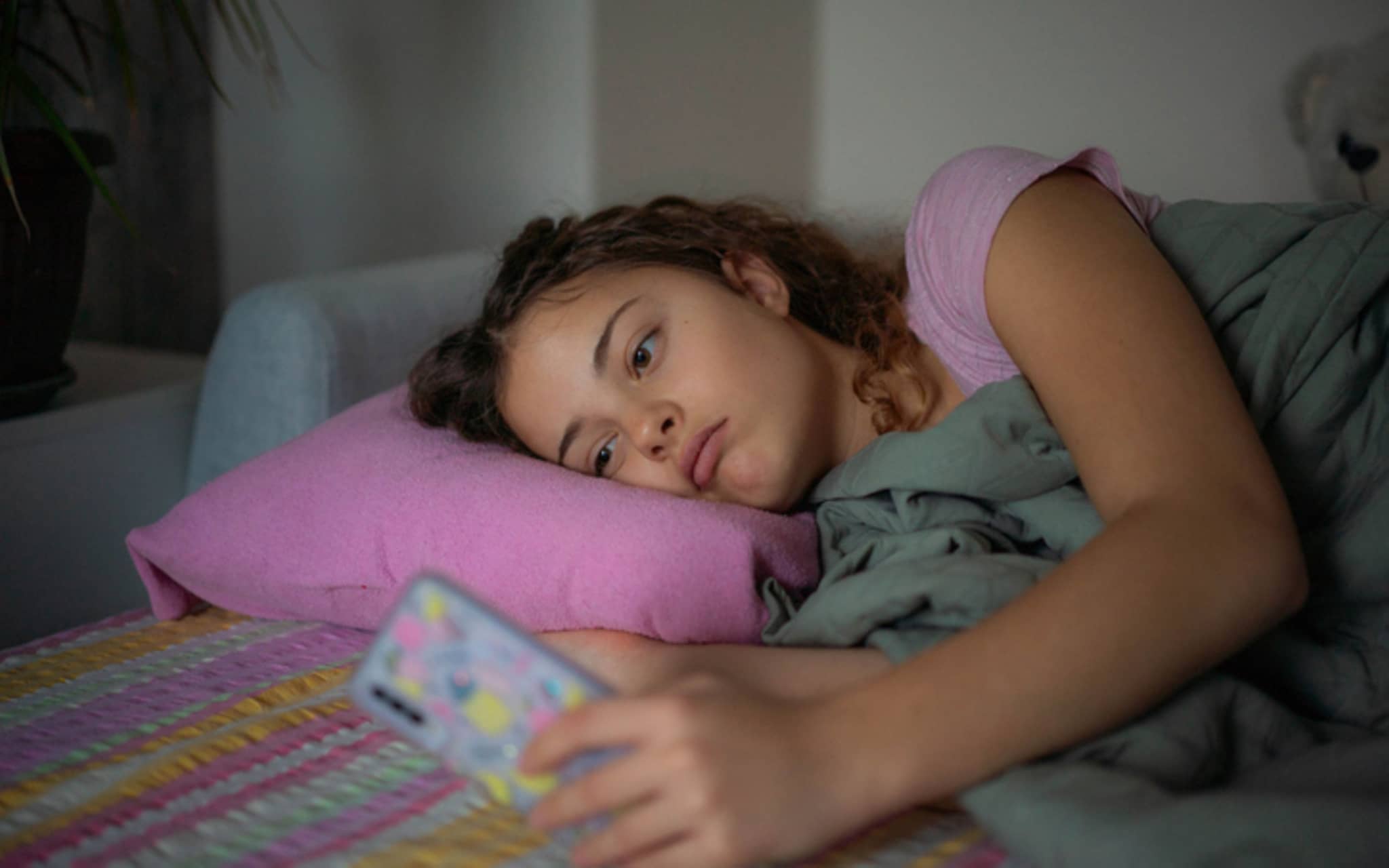 Jugendliche liegt apathisch im Bett und starrt aufs Smartphone.