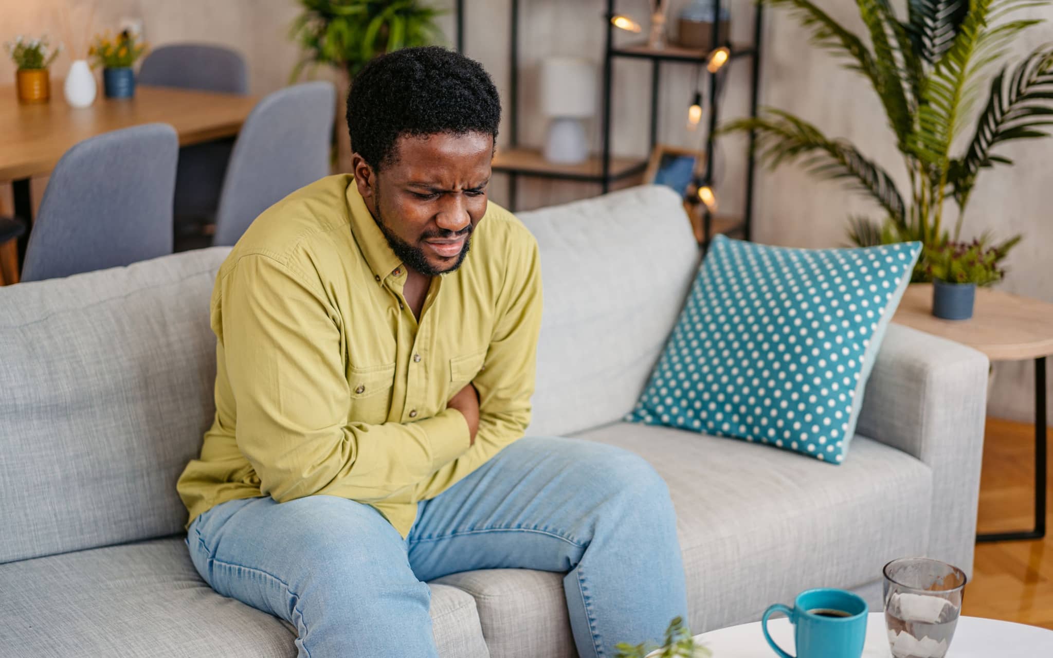 Ein Mann sitzt mit schmerzverzerrtem Gesicht auf einem Sofa und hält sich den Bauch.