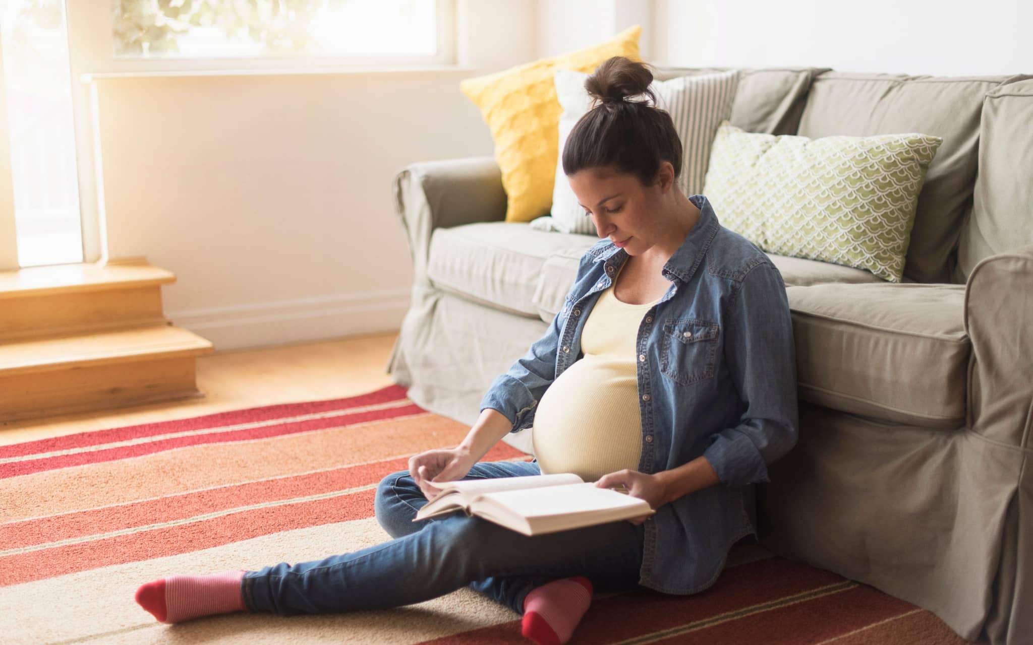 Eine schwangere Frau sitzt vor einem Sofa und liest in einem Buch