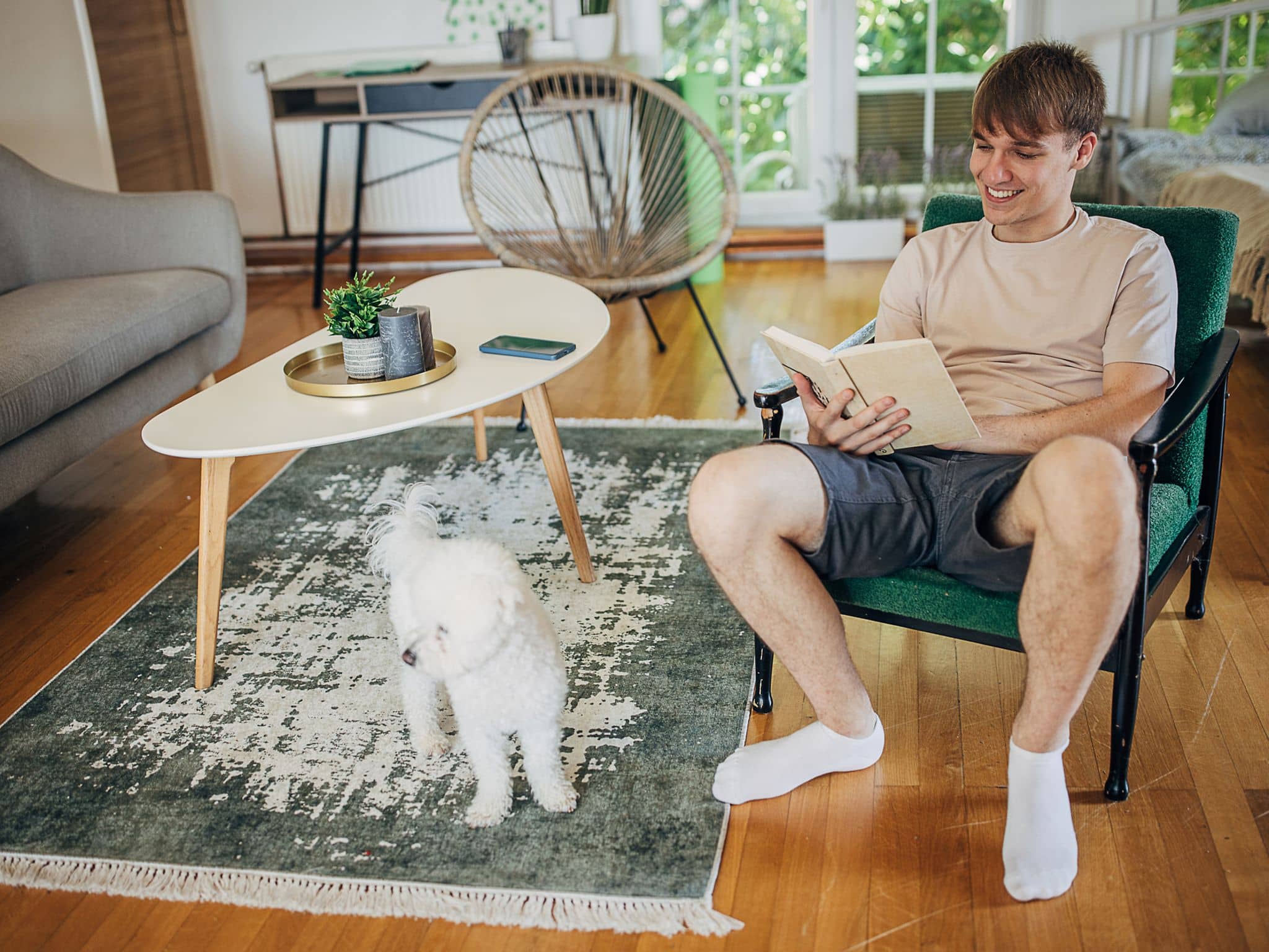Ein junger Mann sitzt im Short in einem Sessel und liest in einem Buch.