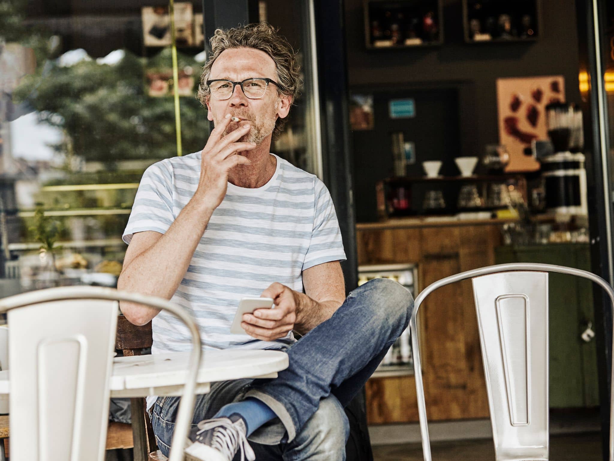 Ein älterer Mann sitzt in einem Café und raucht eine Zigarette.