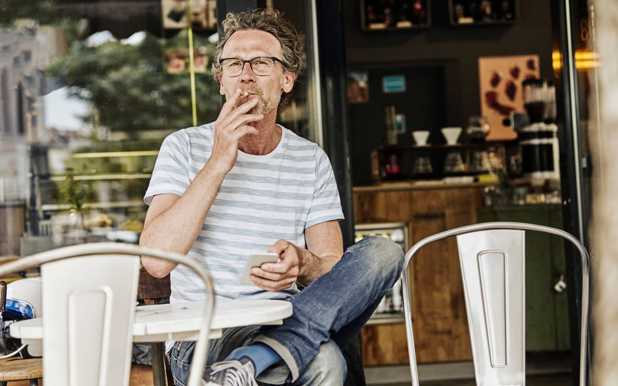 Ein älterer Mann sitzt in einem Café und raucht eine Zigarette.