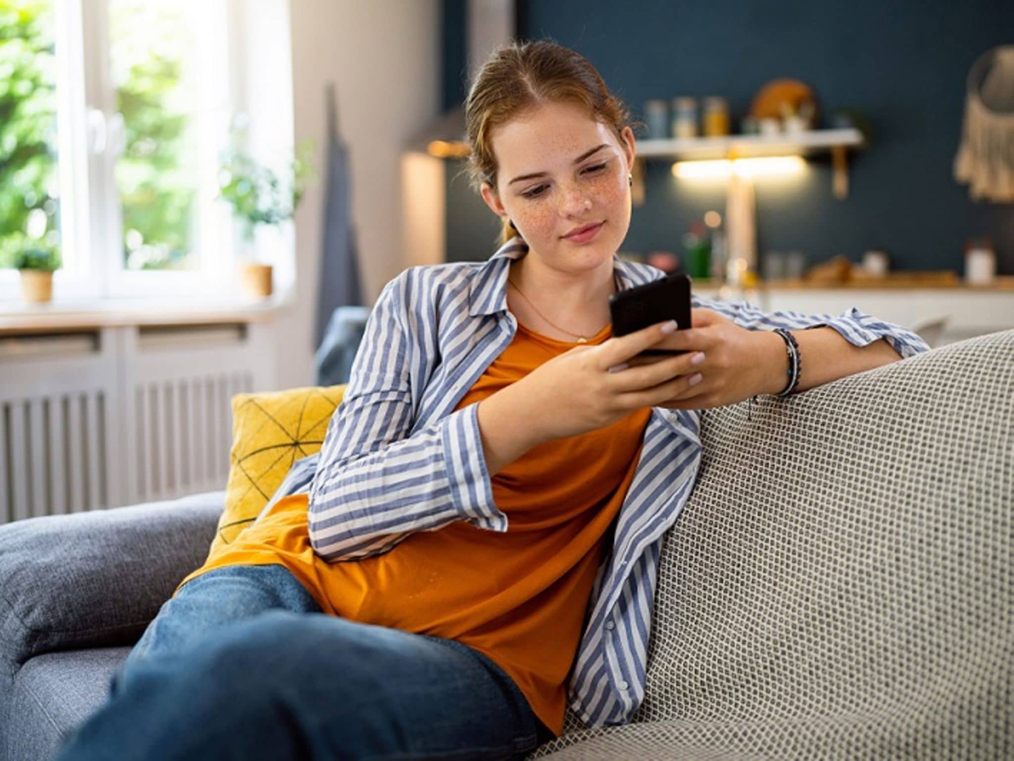 Auszubildene sitzt auf dem Sofa und guckt aufs Handy.