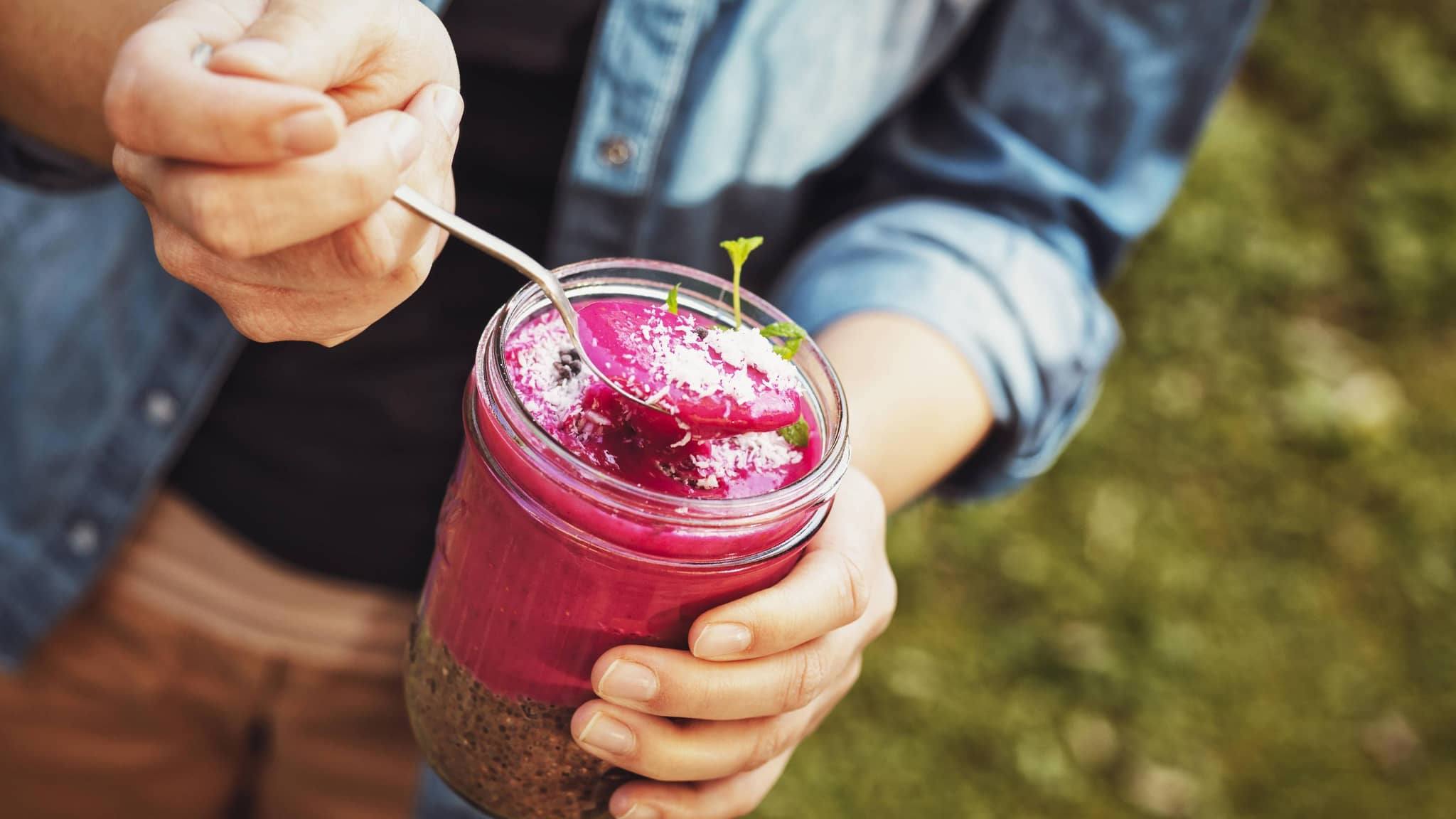 Hände halten ein Glas und einen Löffel mit rotem Dessert und Chia Pudding