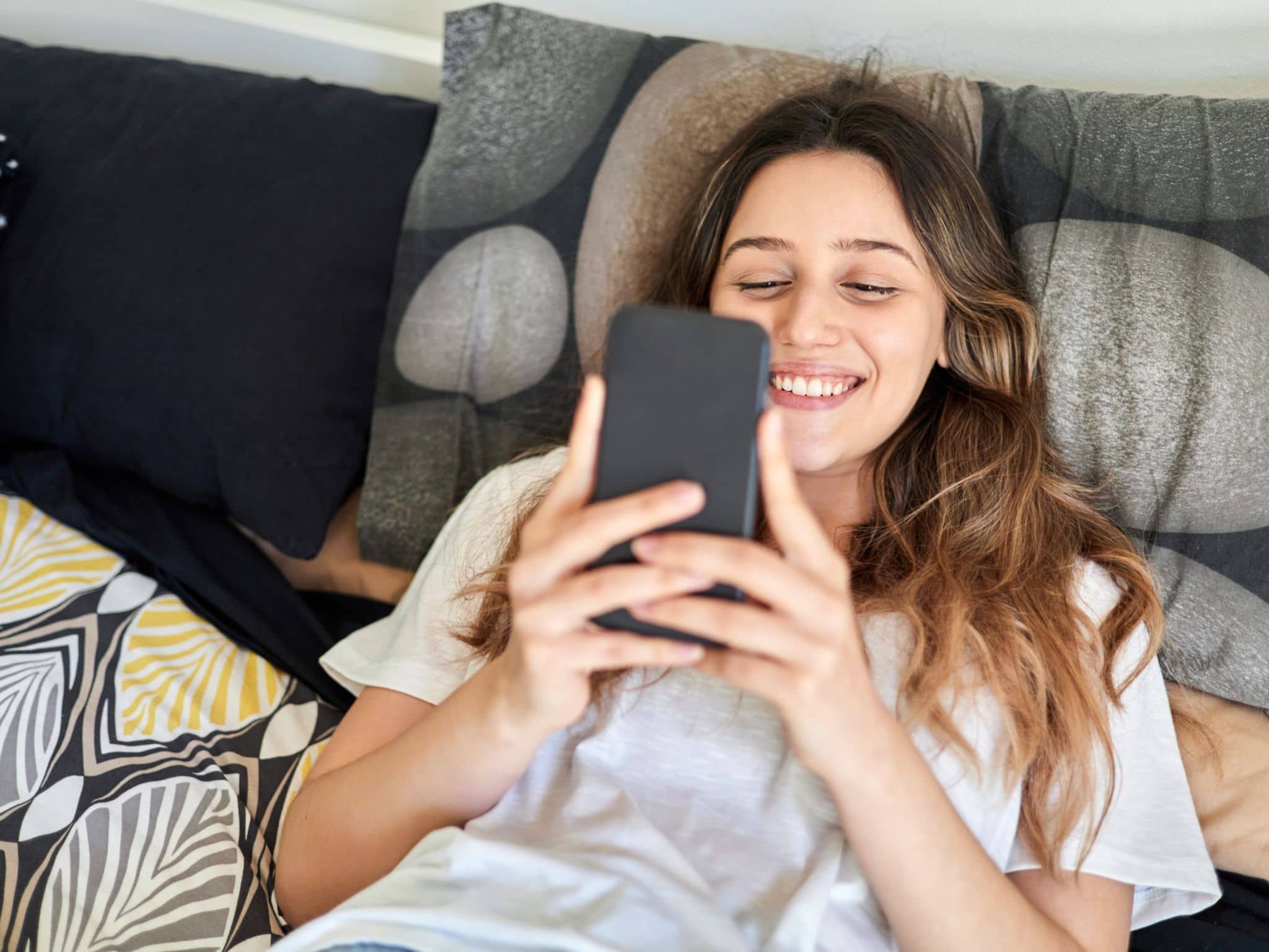 Junge Frau liegt auf dem Sofa und schaut auf ihr Handy.
