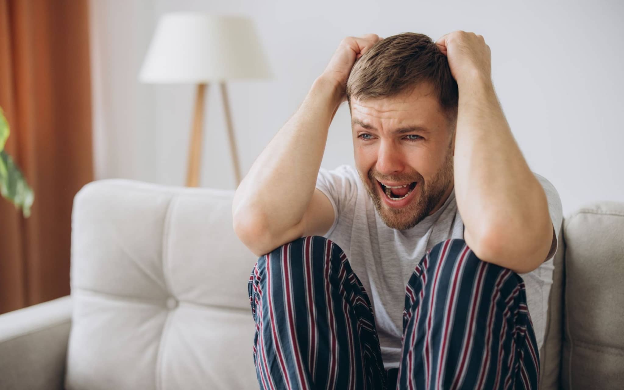 Ein Mann im Pyjama sitzt auf dem Sofa und schreit während einer Psychose.