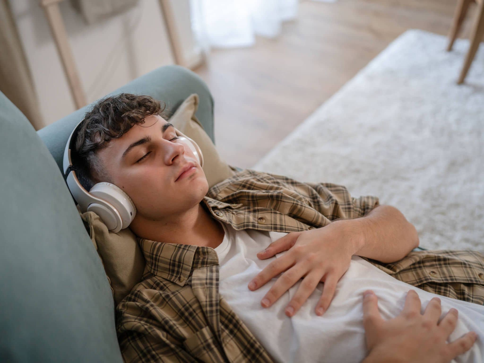 Ein Teenager liegt mit geschlossenen Augen auf der Couch und hört Musik.