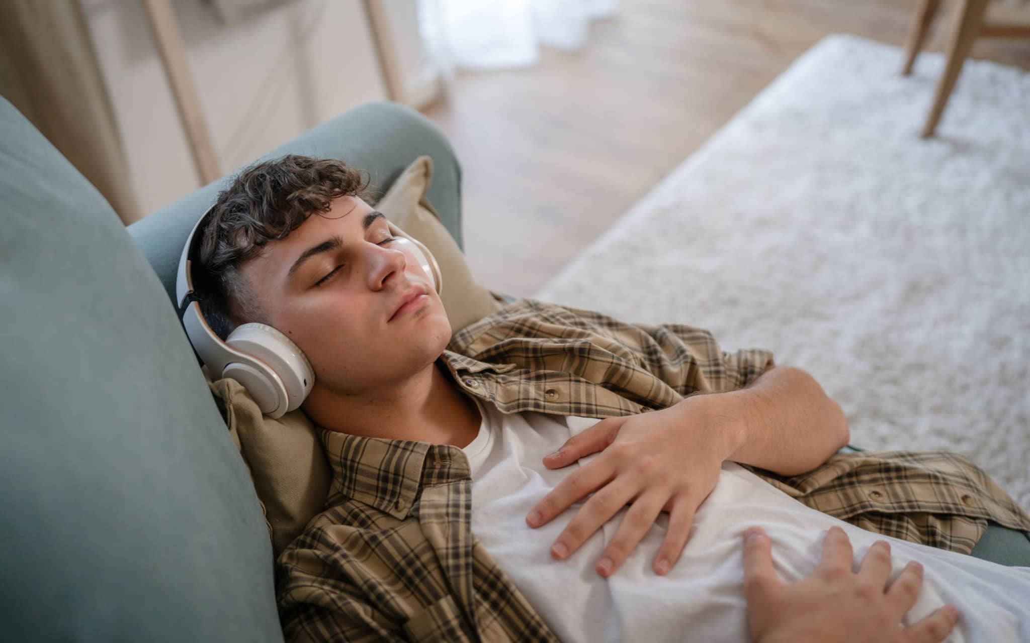 Ein Teenager liegt mit geschlossenen Augen auf der Couch und hört Musik.