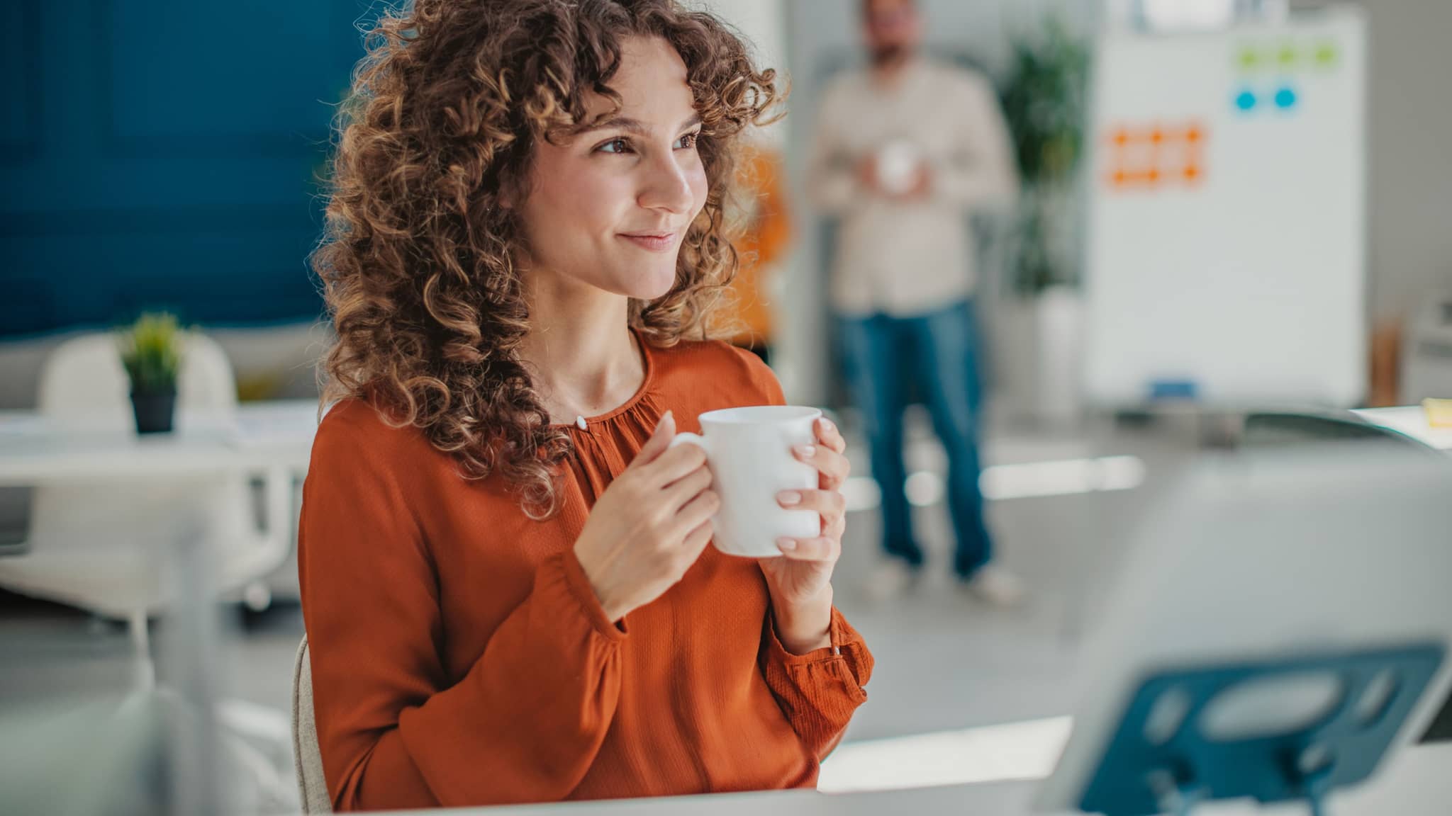 Frau im Büro trinkt entspannt einen Kaffee und lächelt.