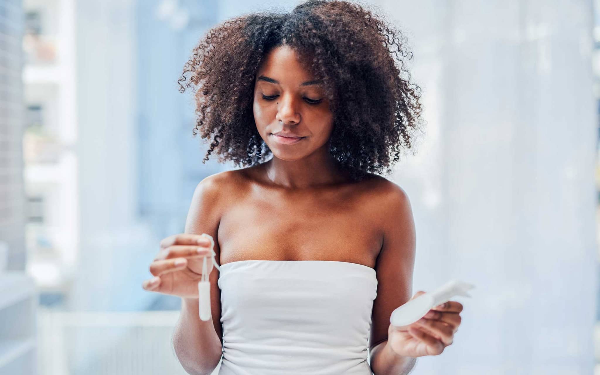 Eine junge Frau hält in der einen Hand ein Tampon hoch, in der anderen eine Binde