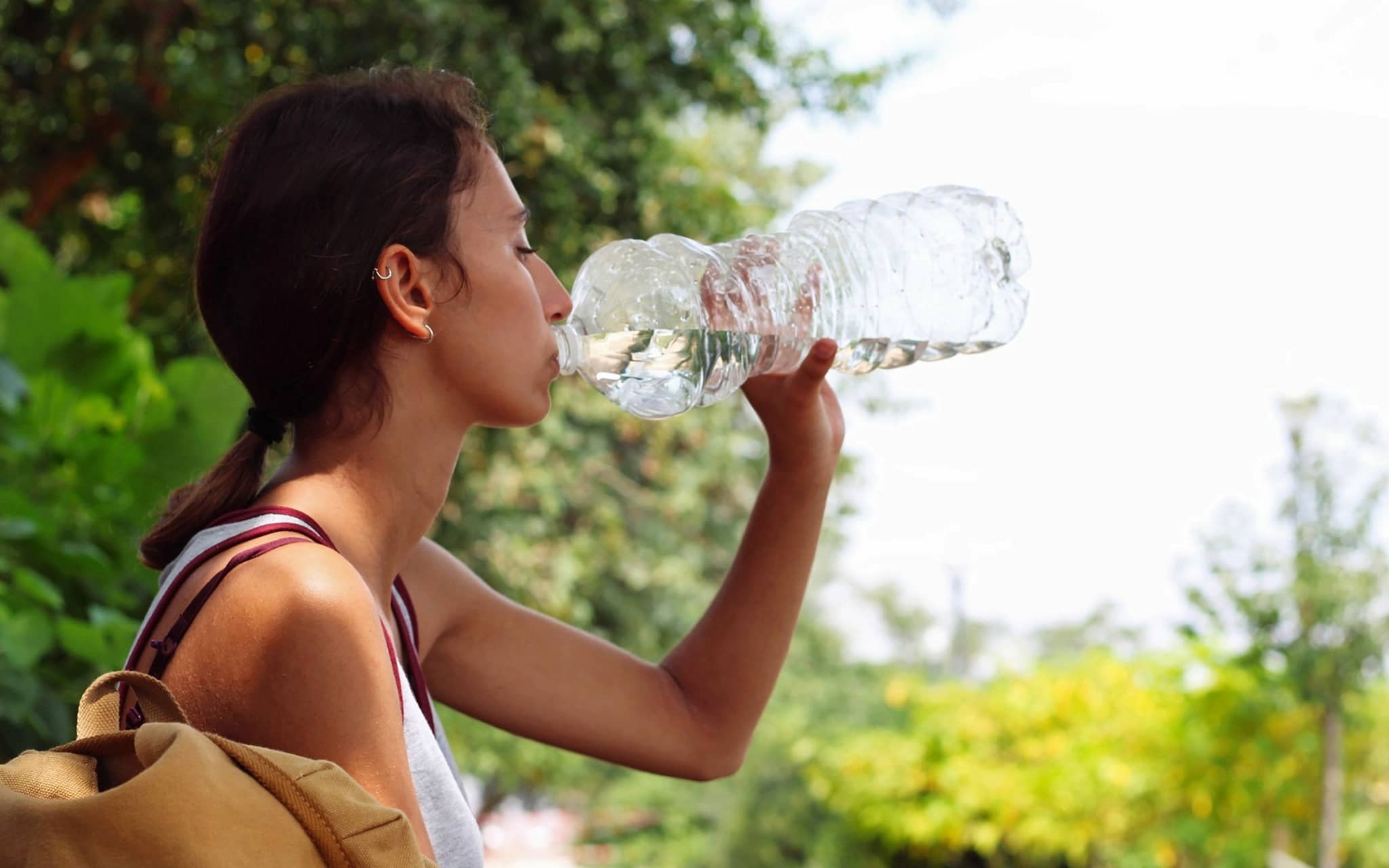 Frau sitzt im Freien und trinkt Wasser aus einer großen Plastikflasche.