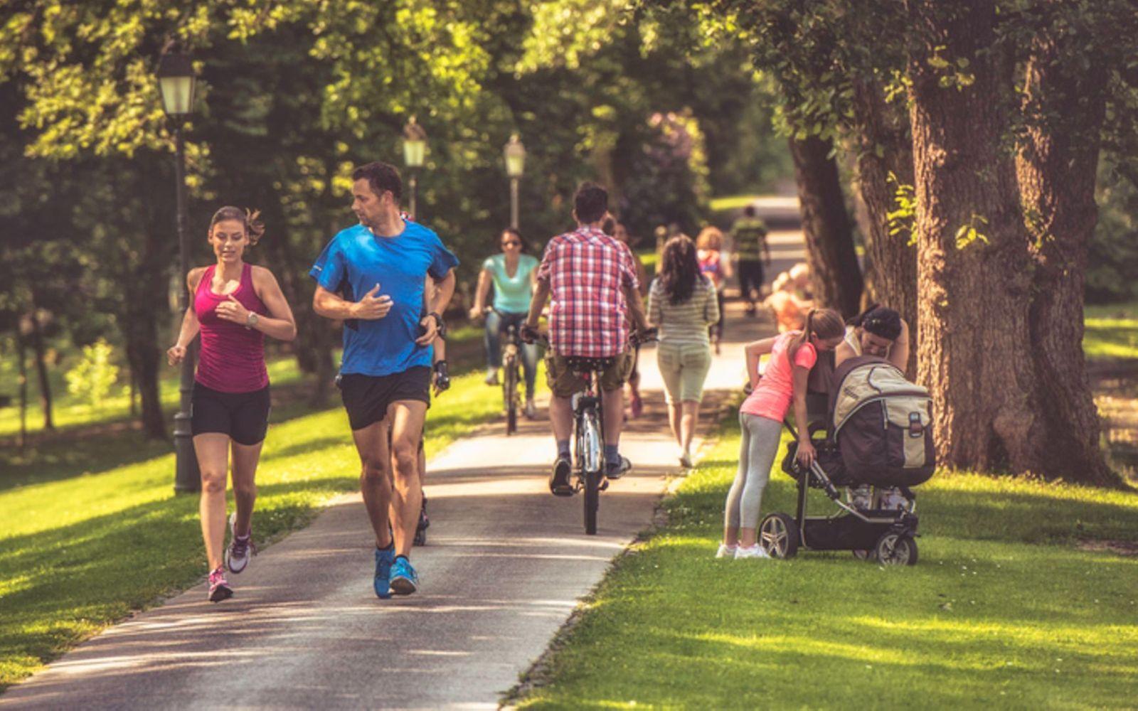 Sport und Gesundheit: Paar joggt an einem sonnigen Tag durch einen belebten Park.