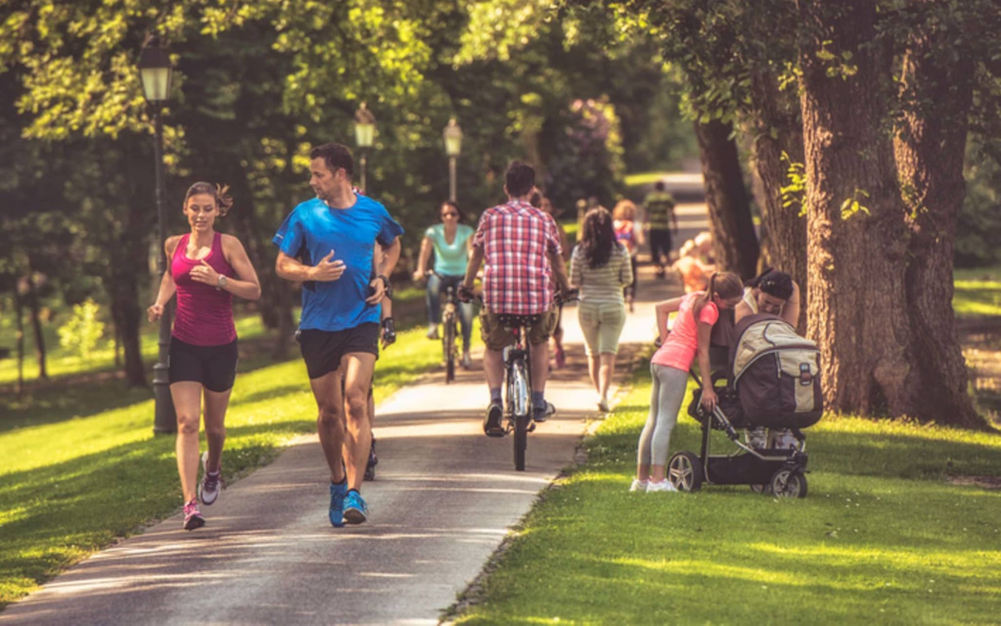 Sport und Gesundheit: Paar joggt an einem sonnigen Tag durch einen belebten Park.