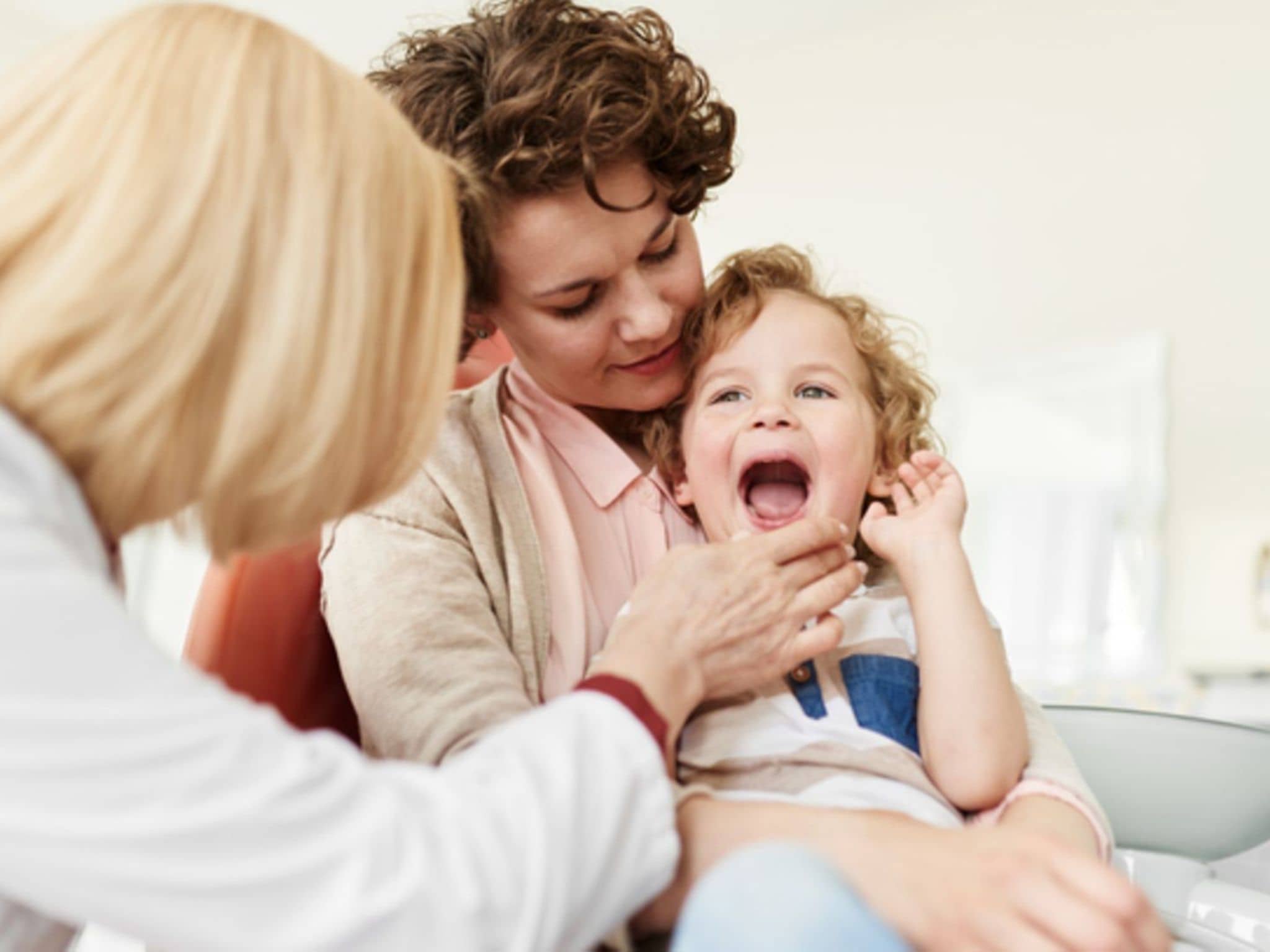 Symbolbild für Angst vorm Zahnarzt: Eine Mutter hat ihr Kind auf den Schoß und die Zahnärztin schaut in den Mund des Kindes