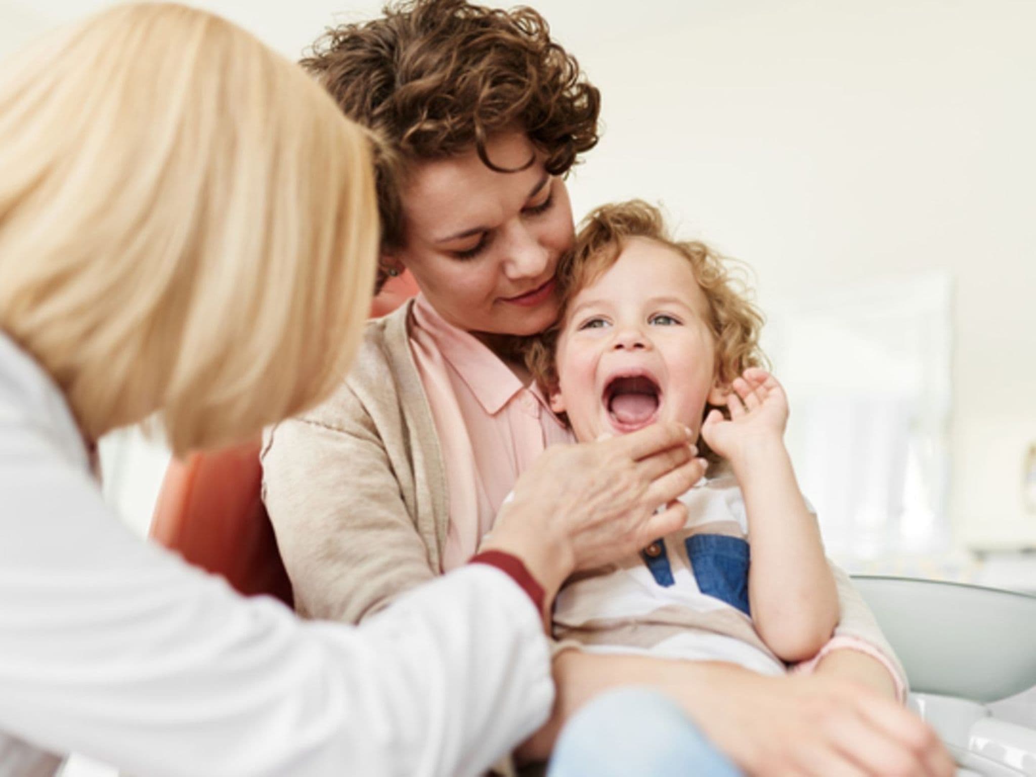 Symbolbild für Angst vorm Zahnarzt: Eine Mutter hat ihr Kind auf den Schoß und die Zahnärztin schaut in den Mund des Kindes
