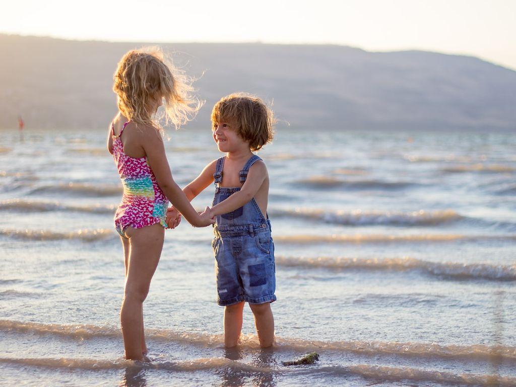 Schöne Erinnerungen an Kindheit: Zwei kleine Kinder stehen am Meer und halten sich an den Händen.