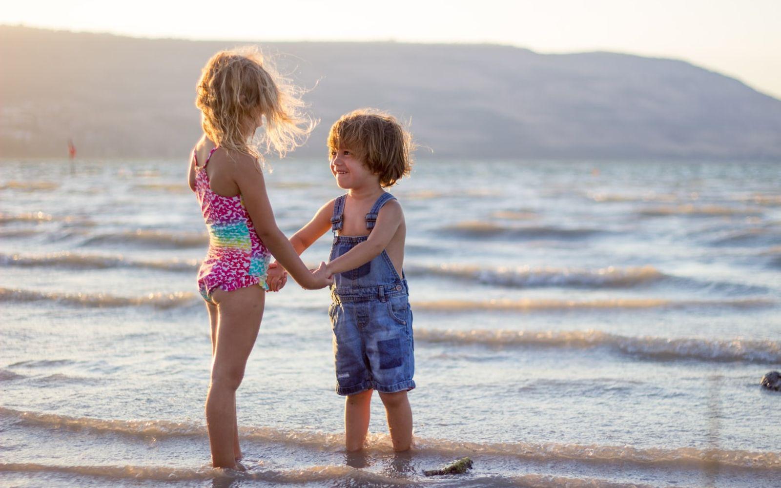 Schöne Erinnerungen an Kindheit: Zwei kleine Kinder stehen am Meer und halten sich an den Händen.
