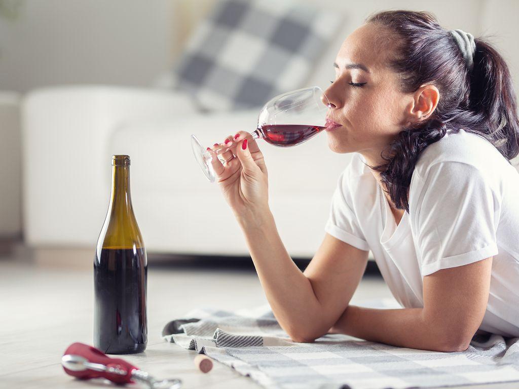 Co-Abhängigkeit: Eine Frau liegt auf dem Fußboden und trinkt Rotwein