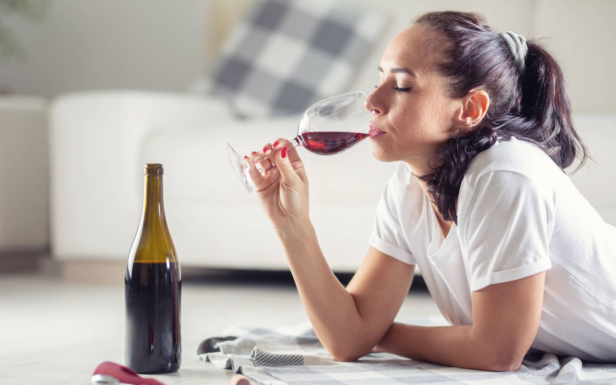 Co-Abhängigkeit: Eine Frau liegt auf dem Fußboden und trinkt Rotwein