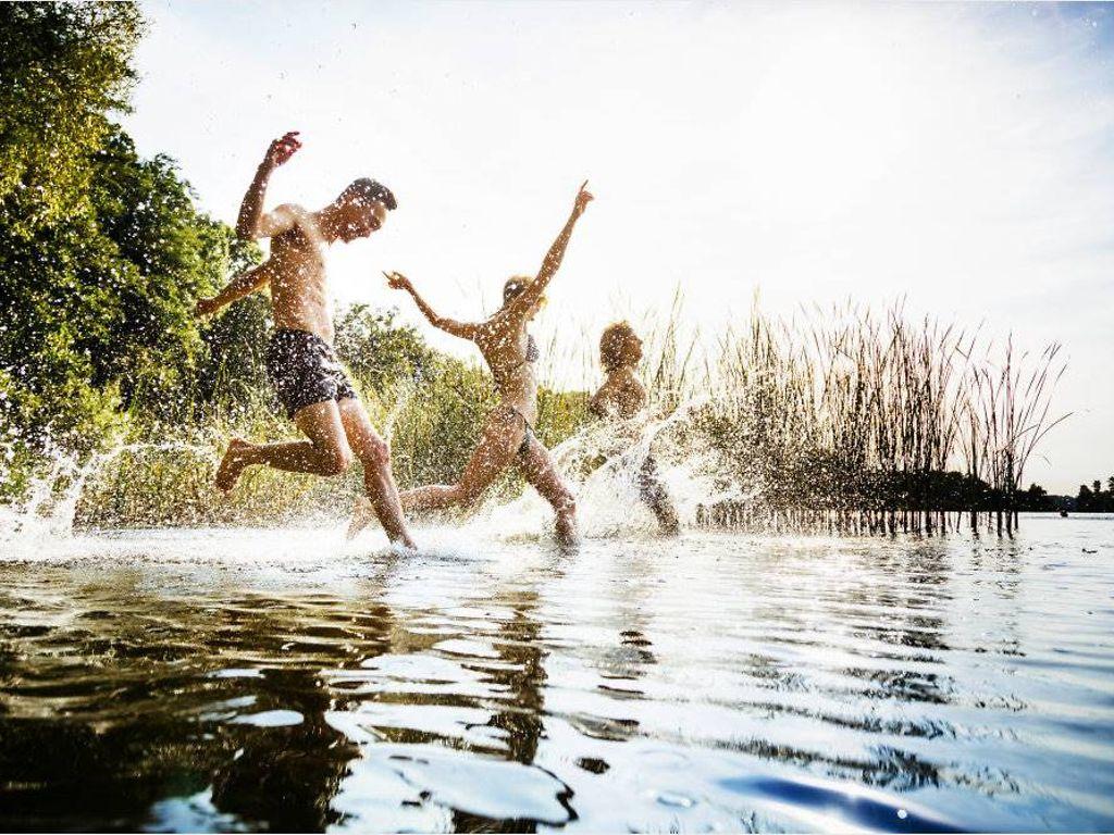 Movement Culture: Eine Gruppe von Freunden, die an einem gemeinsamen Tag am See aufgeregt im Wasser planscht.