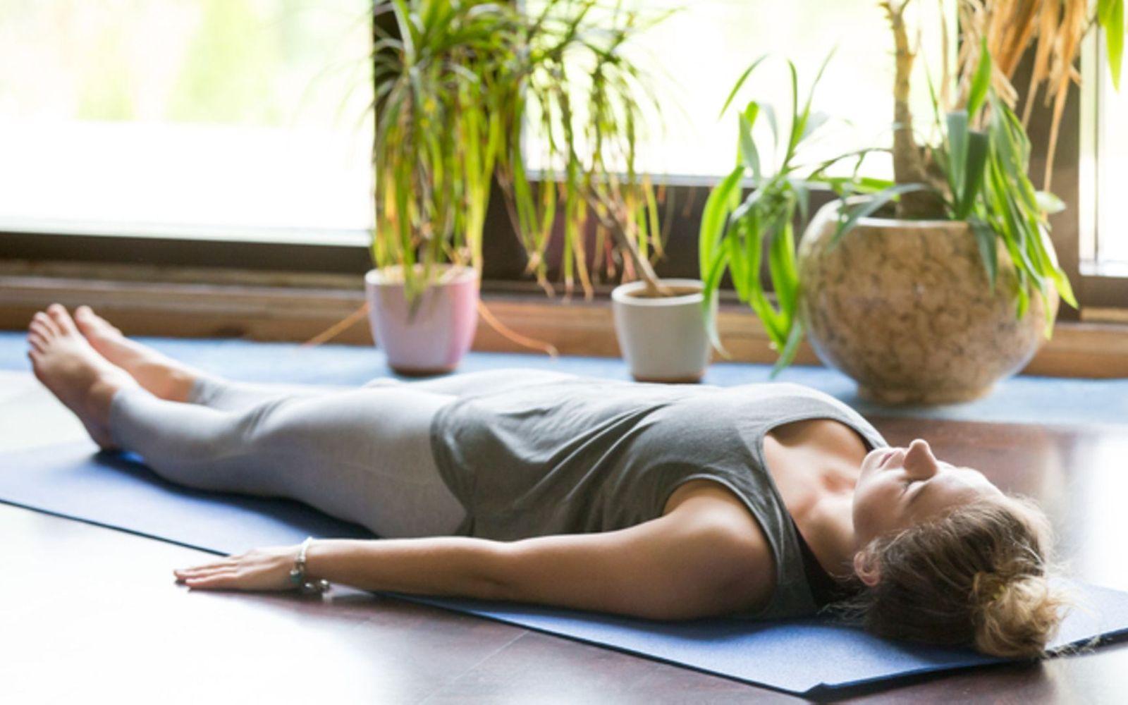 Meditation: Eine Frau liegt entspannt auf dem Fußboden und meditiert.