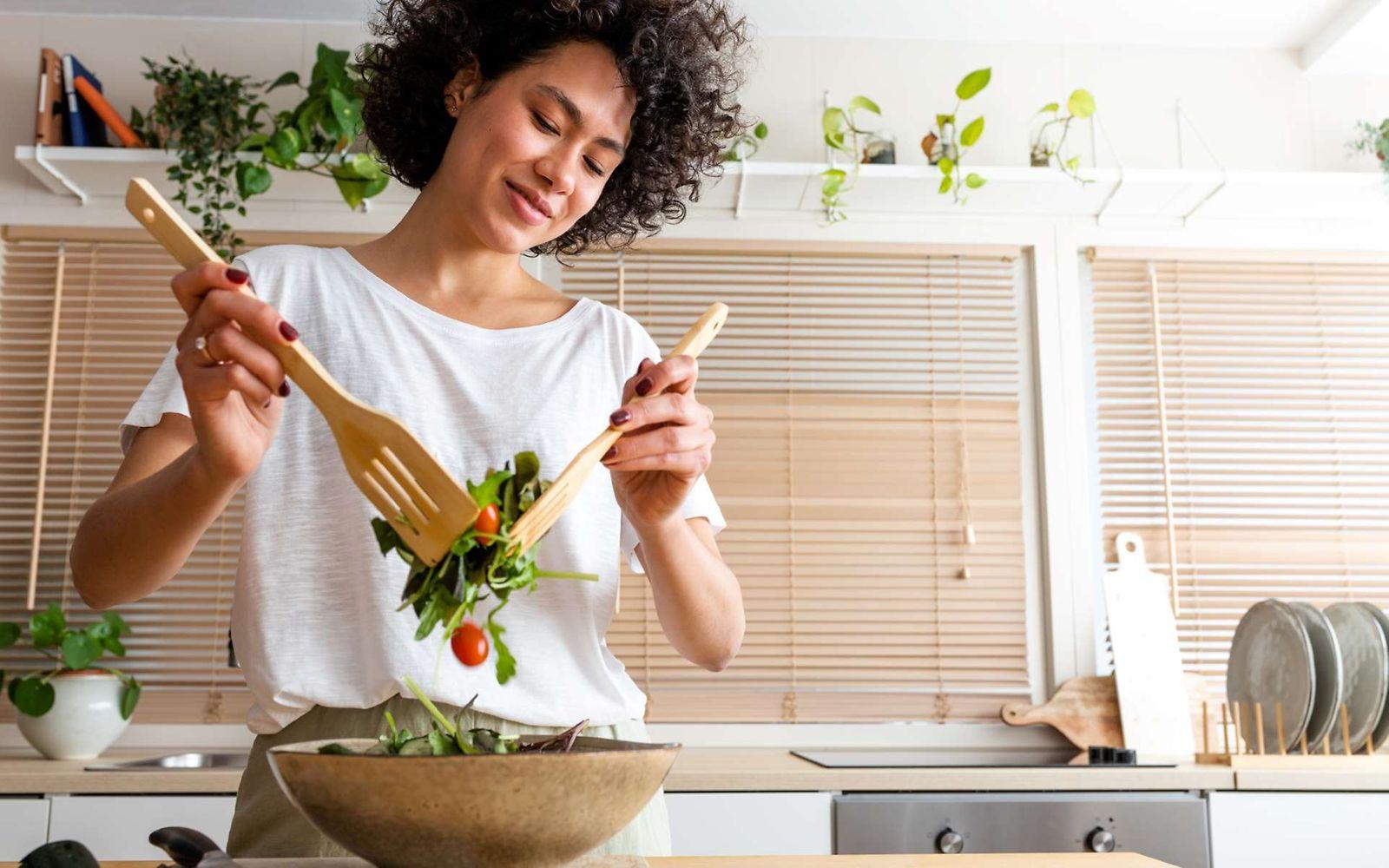 Ernährungs-Tipps: Junge Frau steht in der Küche und bereitet einen Salat zu.
